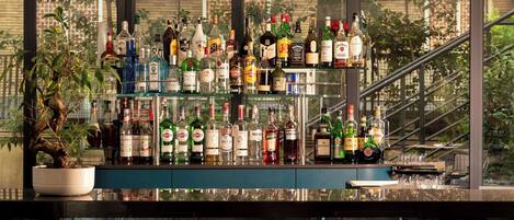 A bar with a variety of liquor bottles and glasses, a potted plant, and a view of a building through large windows.