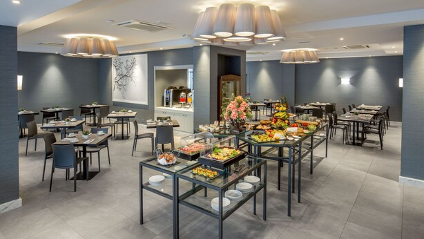 A modern dining area with glass tables, multiple seating options, and a variety of food displays. - Hotel American Palace Eur (Rome)