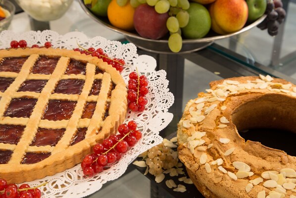 A pie with a lattice crust and red currants on a white doily, next to a bundt cake with almonds. - Hotel American Palace Eur (Rome)