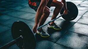 A person performing a deadlift exercise with a barbell on a tiled floor. - Hotel American Palace Eur (Rome)