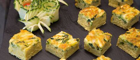 A slate serving board with several square pieces of quiche and a decorative arrangement of vegetables.