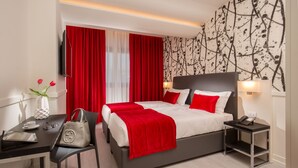 A modern hotel room with a large bed, red accents, a desk with a chair, and a nightstand. - Hotel American Palace Eur (Rome)