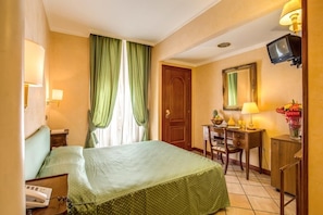 Quarto de hotel com cama, escrivaninha, cadeira, televisão e espelho.