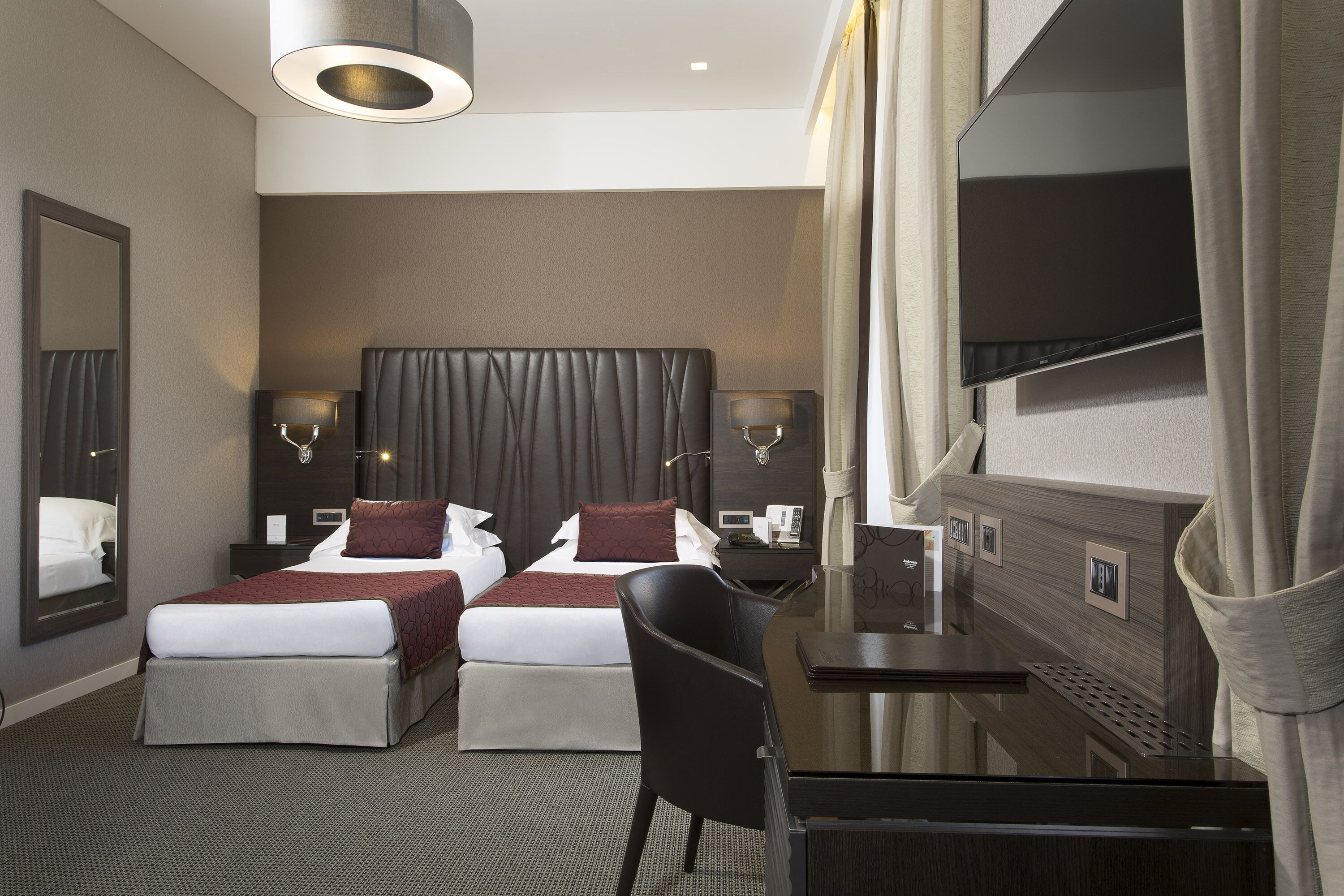 A hotel room with a large bed, two bedside tables, a desk, a chair, a TV, and a mirror.