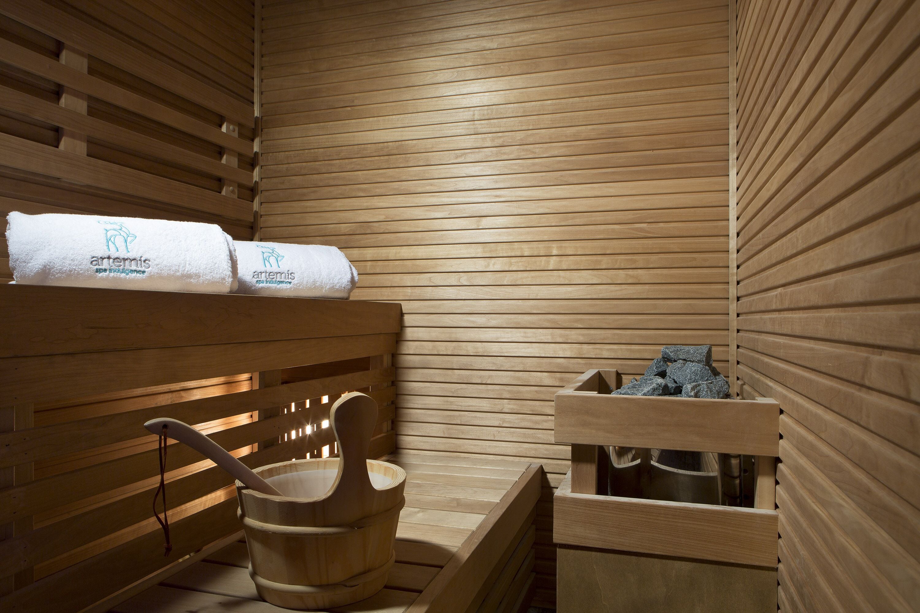 Un sauna con bancos de madera, toallas y un cubo de madera.