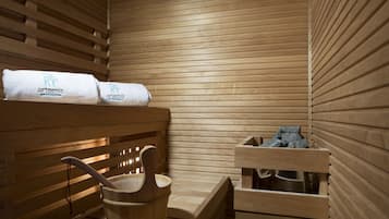 Un sauna con bancos de madera, toallas y un cubo de madera.