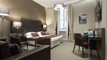 Habitación de hotel con cama, escritorio, silla, lámpara y ventana con cortinas.