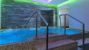 A hot tub with steps and metal railings, surrounded by mosaic-tiled walls and a stone-like textured wall. - Hotel Artemide (Rome)