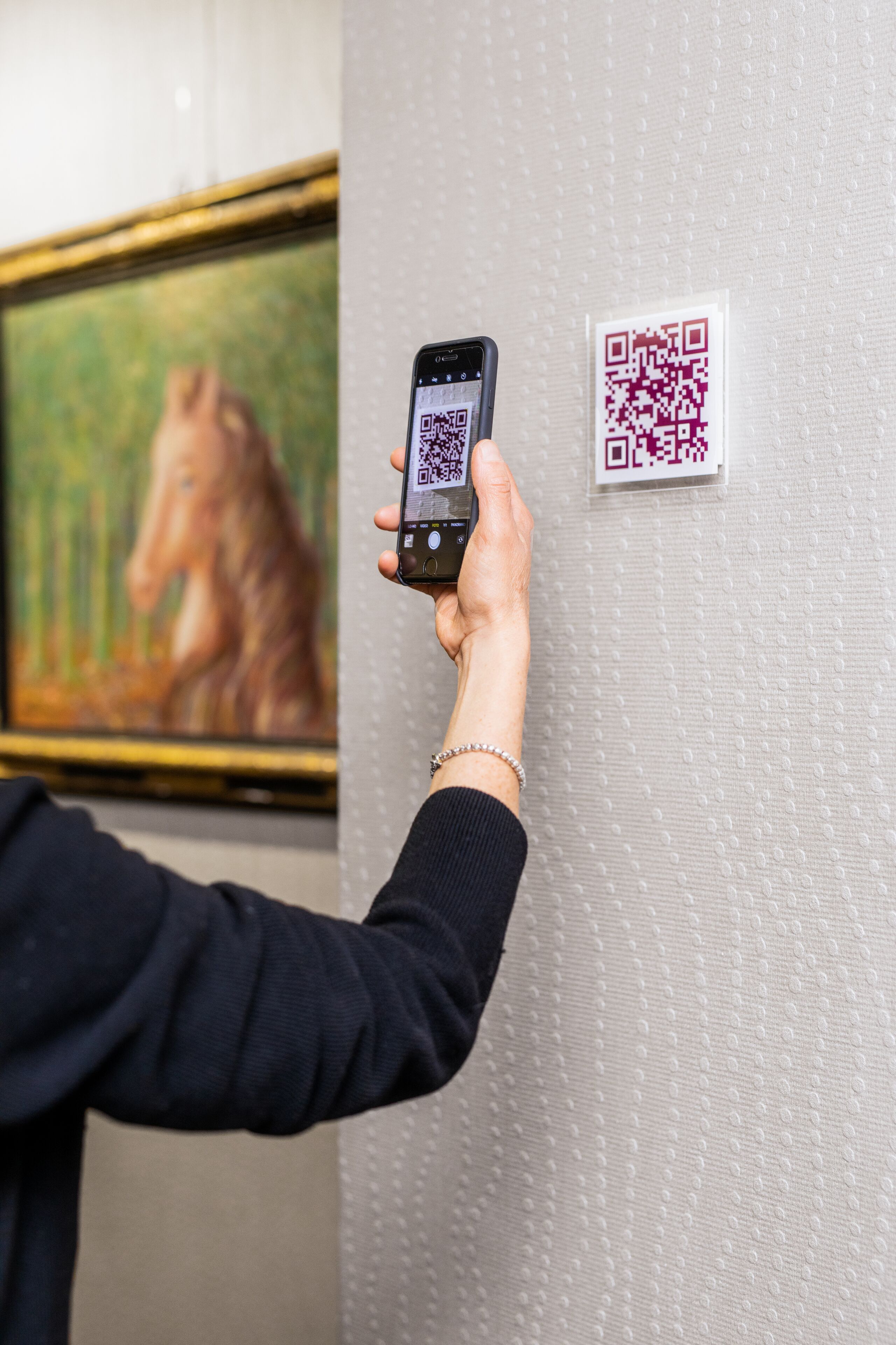 Een persoon houdt een smartphone vast, waarop een QR-code op een structuurwand wordt getoond.