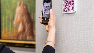 Een persoon houdt een smartphone vast, waarop een QR-code op een structuurwand wordt getoond.