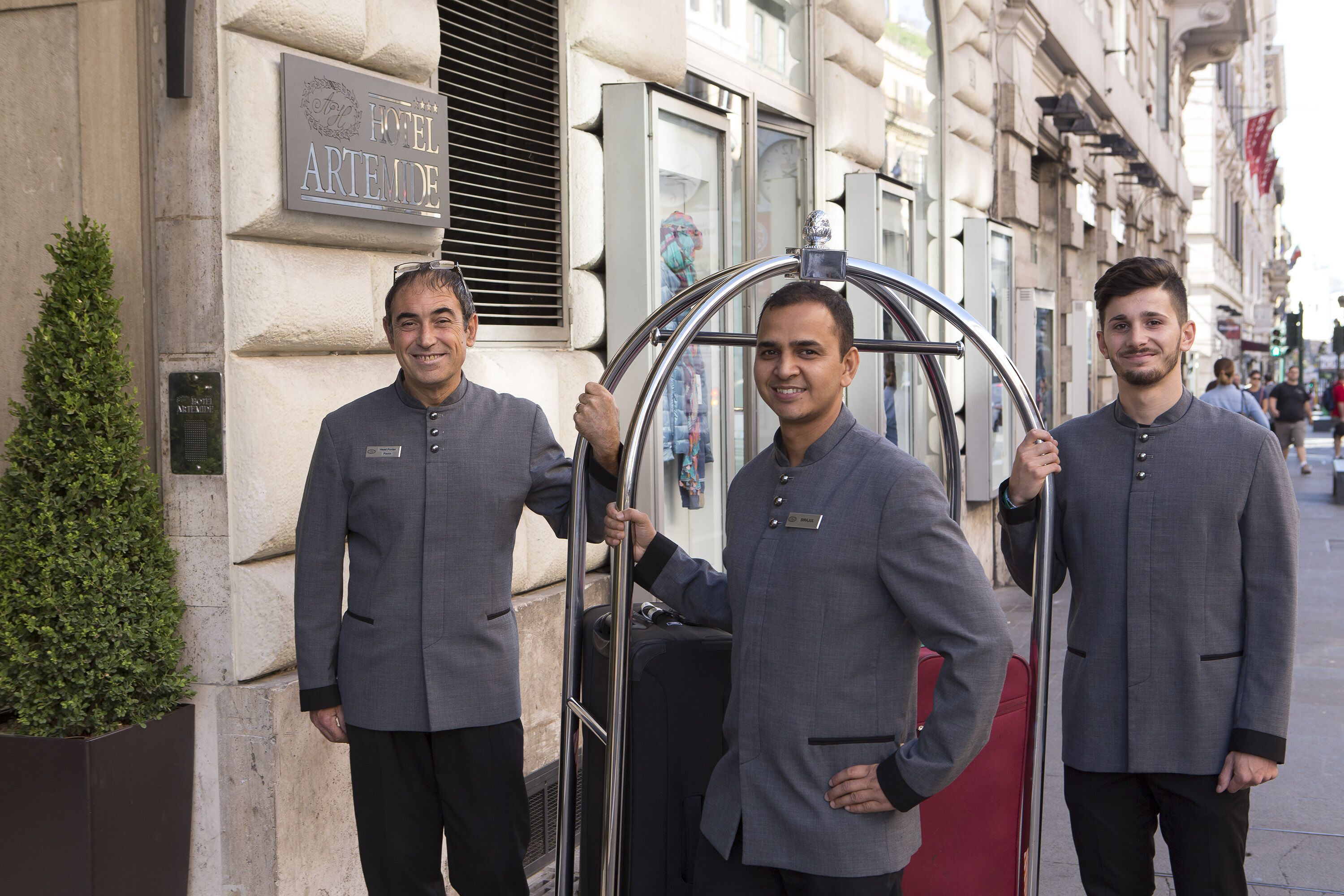 Three men in suits standing by a hotel entrance with a sign that reads "HOTEL ARTEMIDE".