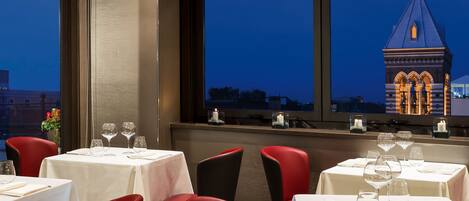 A restaurant with tables set for dining, a view of a tower, and red chairs.