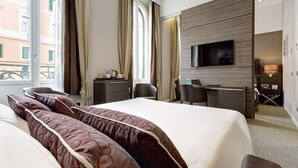 A hotel room with a large bed, a desk, a chair, a television, and a window with curtains.