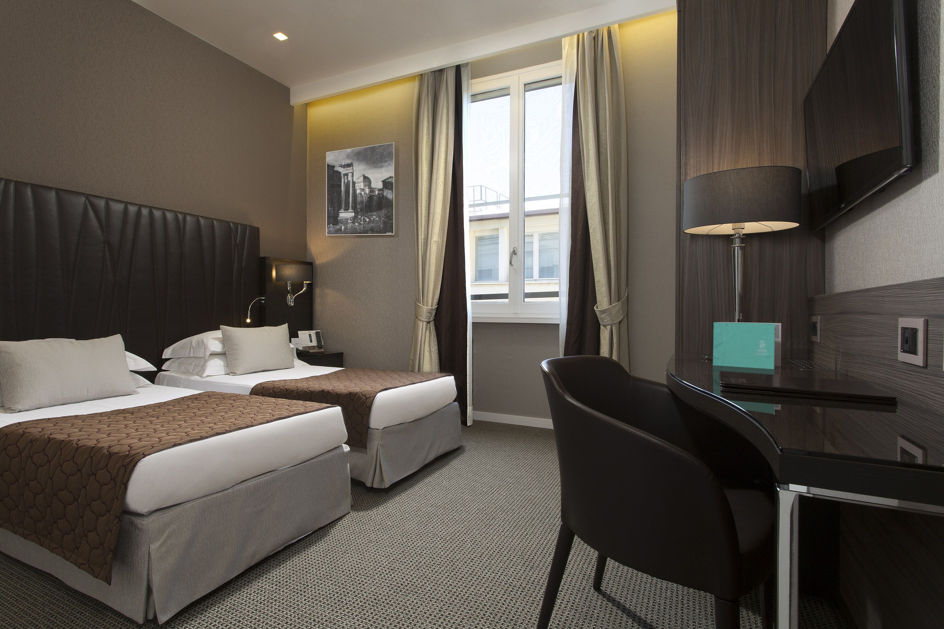 A hotel room with two beds, a desk, a chair, a TV, and a window with curtains.