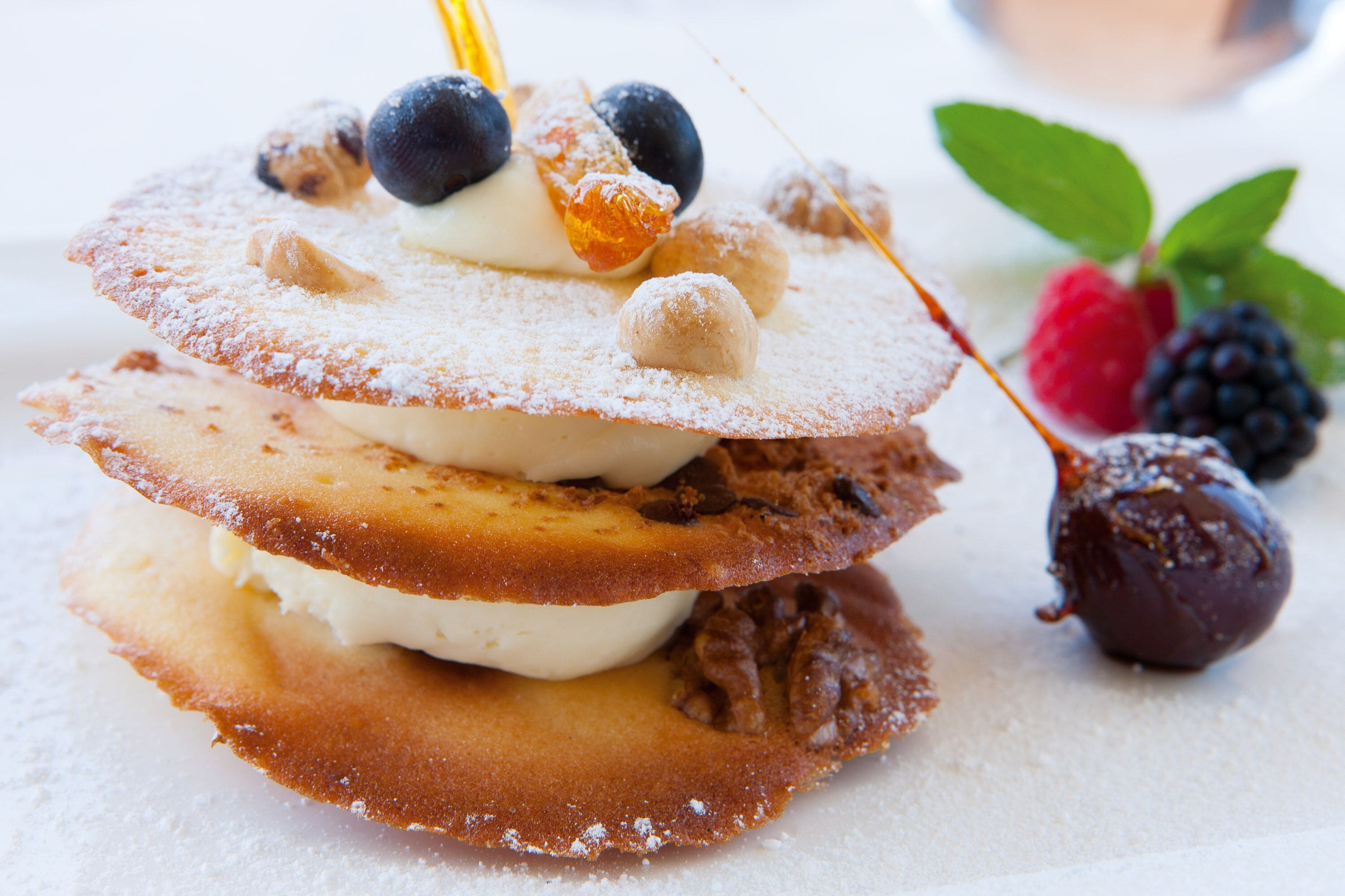 A stack of pancakes with blueberries, powdered sugar, and a chocolate ball.