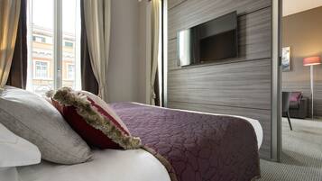 A hotel room with a large bed, a flat-screen TV mounted on the wall, and a view of the city through the window.