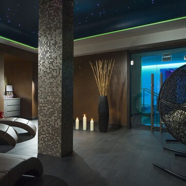 A modern spa area with reclining chairs, a mosaic pillar, candles, and a large decorative vase.
