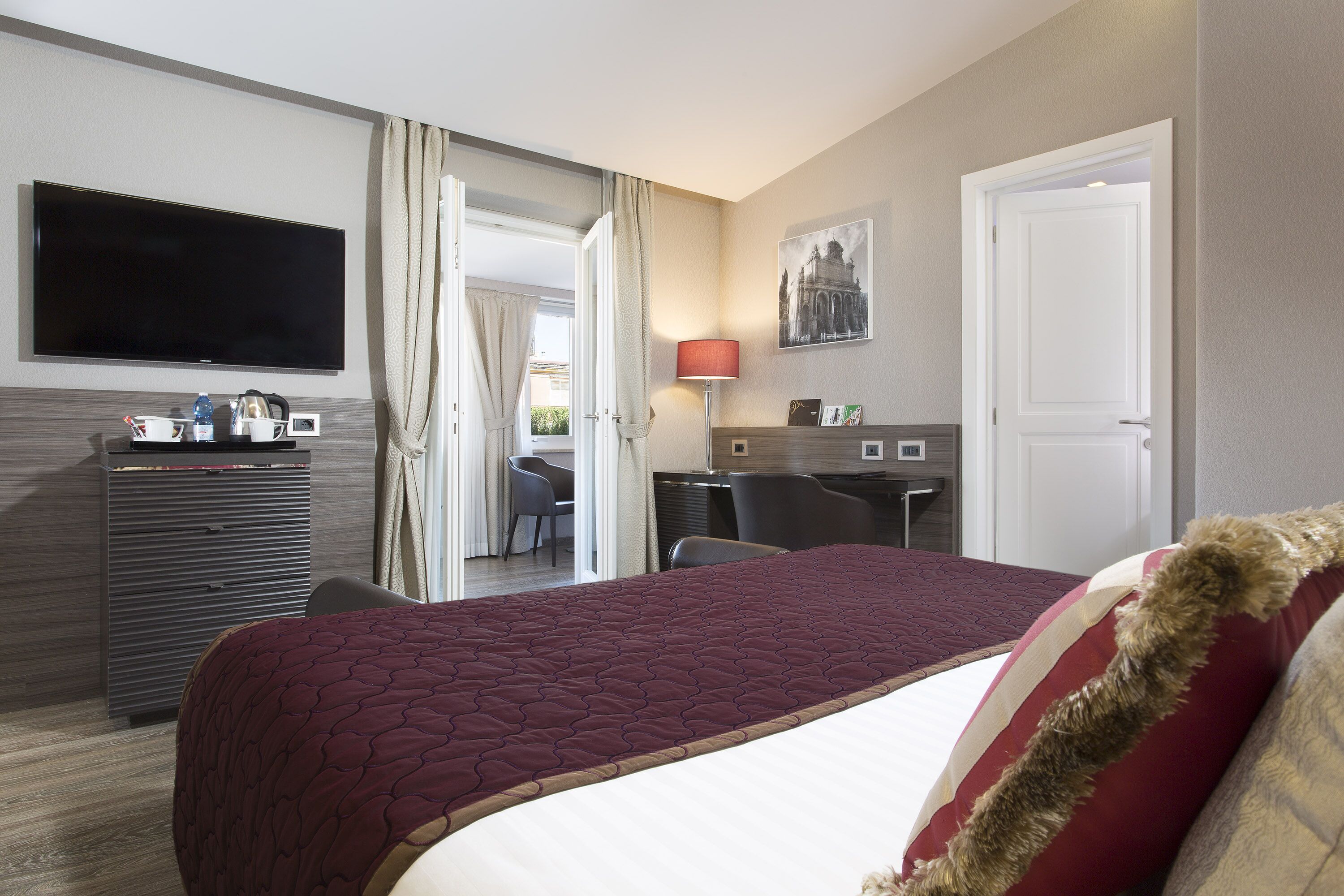 A hotel room with a large bed, a desk, a TV, and a view of the outside.