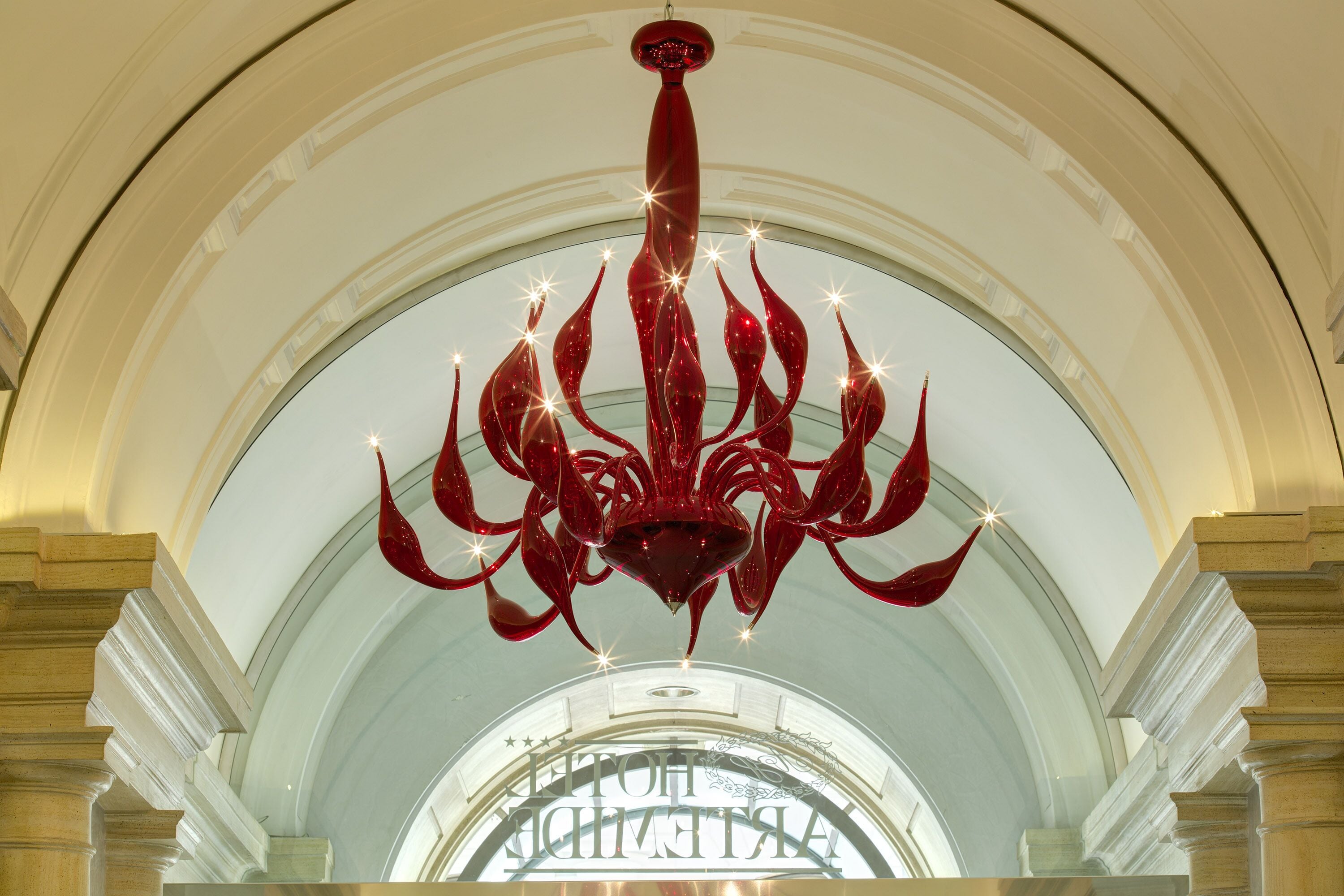 A grand chandelier in a spacious hall with an arched ceiling and a large, ornate entrance.