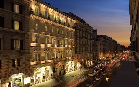 A historic building with multiple stories, ornate architectural details, and a street in front with cars and illuminated storefronts.