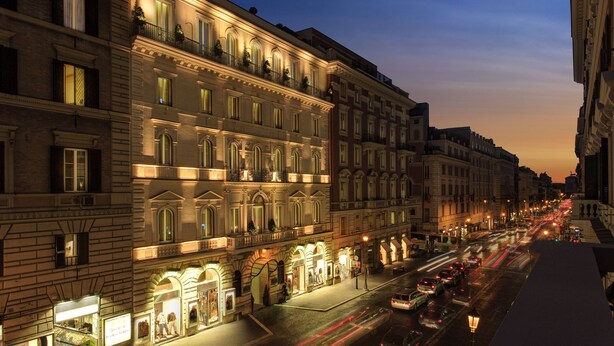 A historic building with multiple stories, ornate architectural details, and a street in front with cars and illuminated storefronts. - Hotel Artemide (Rome)