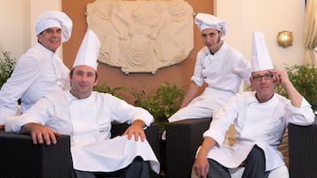 Cuatro chefs sentados en sillas de mimbre en una habitación con un relieve de piedra en la pared.