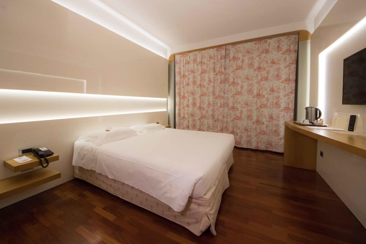 A modern hotel room with a large bed, bedside table, and a desk with a coffee maker.