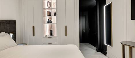 Un dormitorio moderno con una cama grande, un armario con estantes iluminados, una mesita de noche y una lámpara auxiliar.
