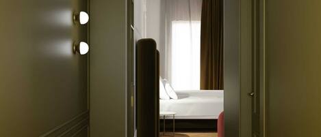 A hotel room with a bed, a mirror with lights, a window with curtains, and a wooden floor.