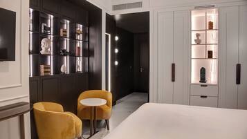 A hotel room with a bed, two chairs, a small table, and a built-in bookshelf with decorative items.