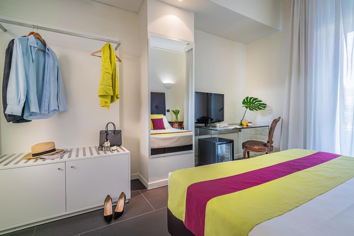 A hotel room with a bed, a desk, a TV, a mirror, and a wardrobe.