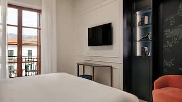 Une chambre d’hôtel avec un lit, un téléviseur fixé au mur, une petite table, une chaise et une vue sur l’extérieur.
