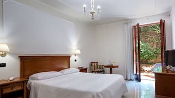 A hotel room with a large bed, bedside lamps, a desk with a telephone, a chair, a small table with a laptop and a drink, and a TV.