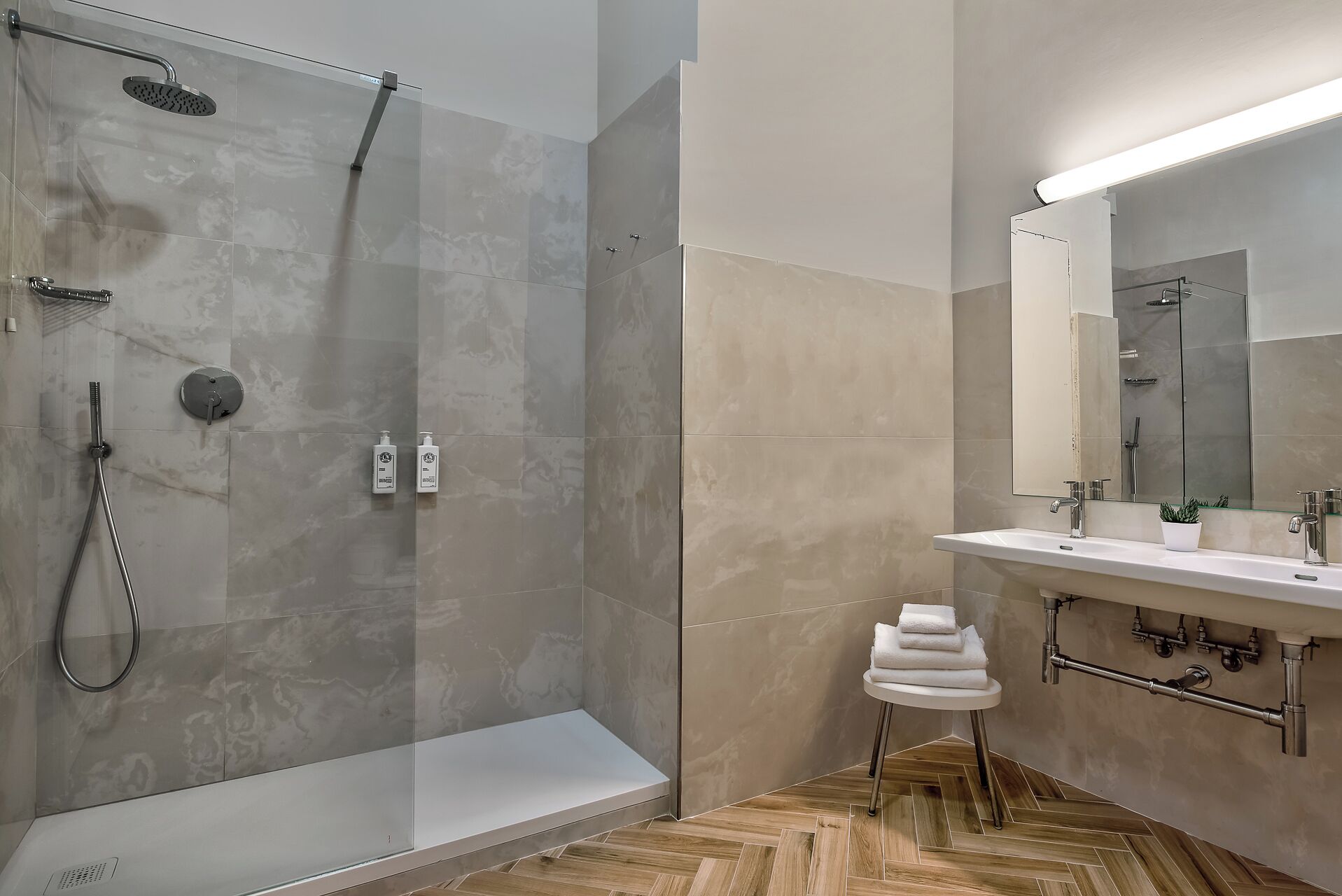 A modern bathroom with a glass-enclosed shower, a vanity with a mirror, and a herringbone wood floor.