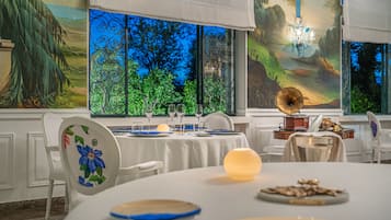 A dining area with a table set for two, featuring a decorative plate, a candle, and a small dish of nuts.