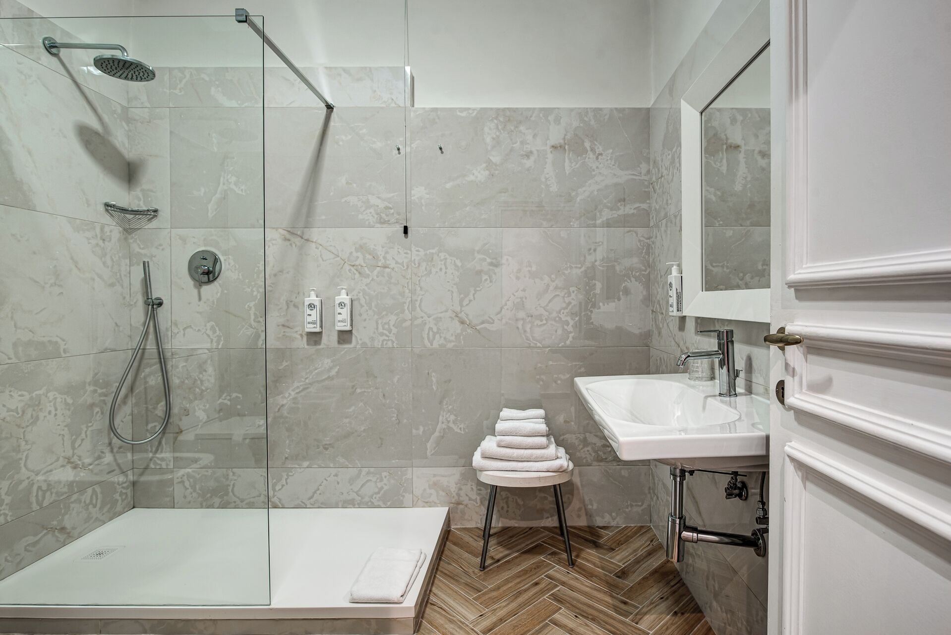 A modern bathroom with a glass-enclosed shower, a white sink, and a herringbone-patterned floor.