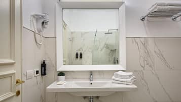 Un baño con lavamanos blanco, espejo, secador de pelo montado en la pared y toallero.