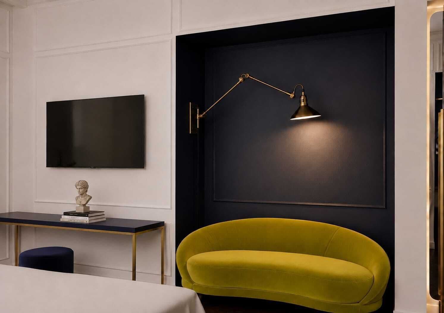 A modern room with a black accent wall, a mounted flat-screen TV, a desk with a bust sculpture, a yellow armchair, and a floor lamp.