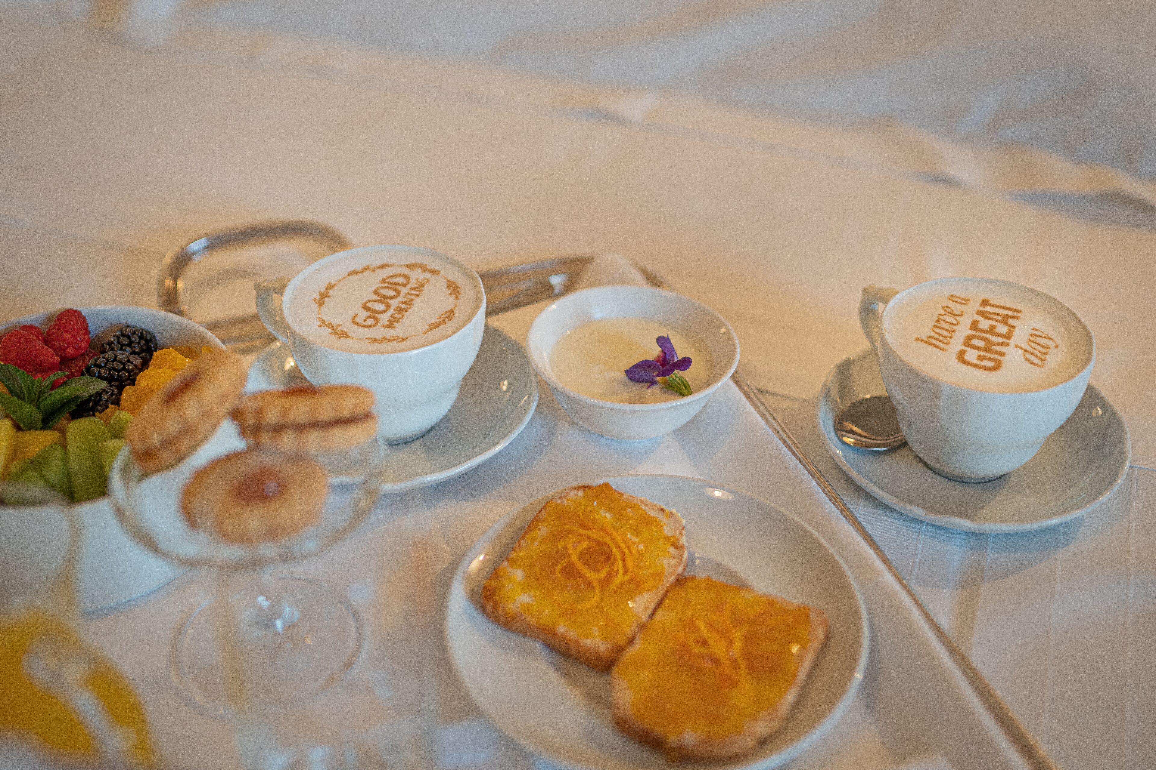 A breakfast setting with coffee cups, pastries, and a fruit bowl.