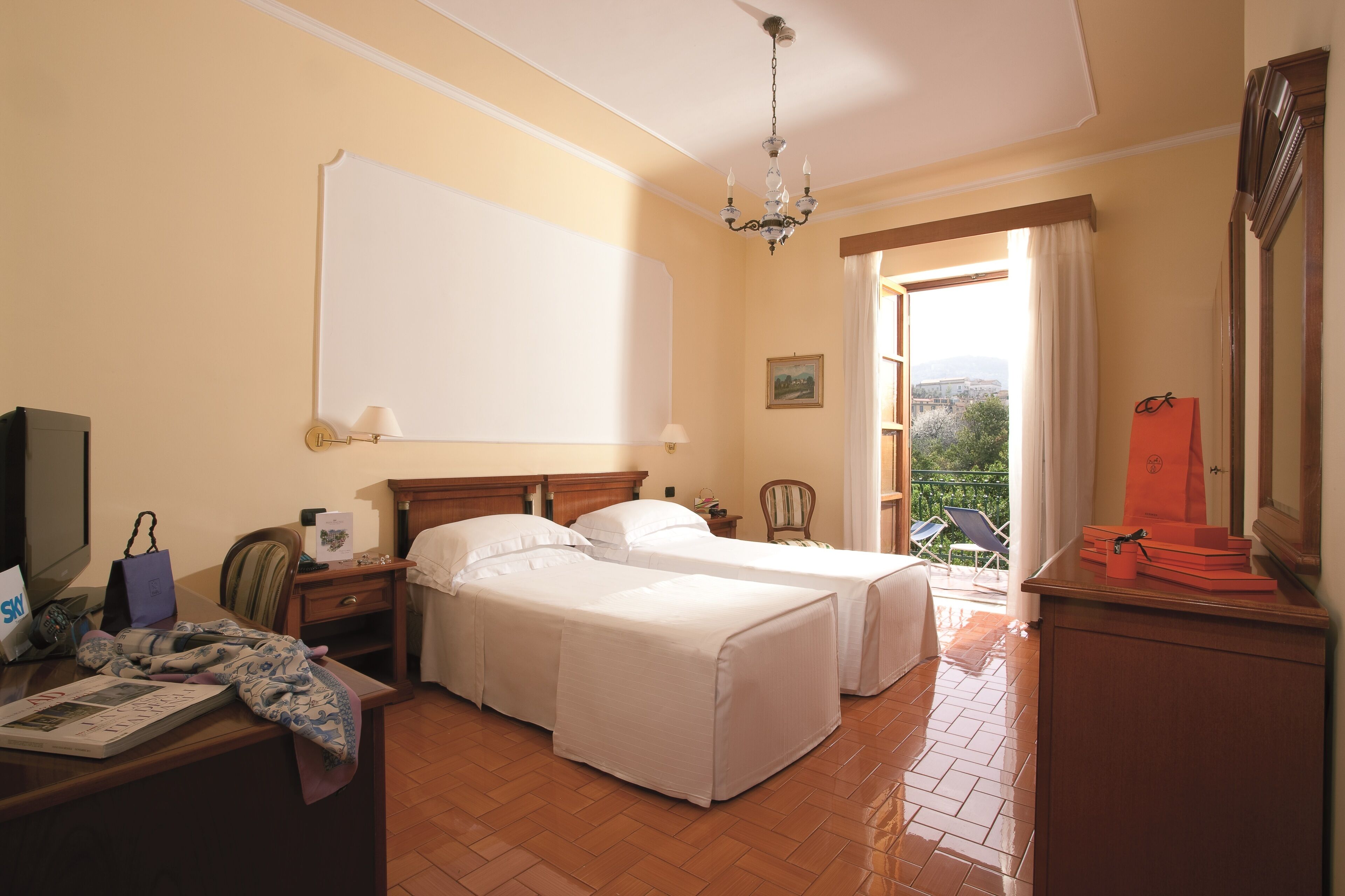 Habitación de hotel con dos camas, un escritorio con computadora, una silla, armario y balcón con vistas.
