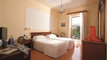 Habitación de hotel con dos camas, un escritorio con computadora, una silla, armario y balcón con vistas.