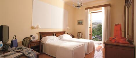 A hotel room with two beds, a desk with a computer, a chair, a wardrobe, and a balcony with a view.