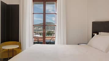 A hotel room with a bed, a small round table, a yellow chair, and a balcony with a view of a mountain.