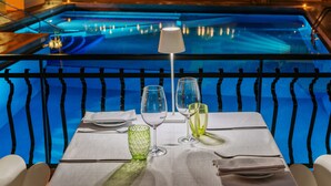 A dining table with a white tablecloth, two wine glasses, and a green glass on a balcony overlooking a pool. - Majestic Palace Hotel (Sant'Agnello)