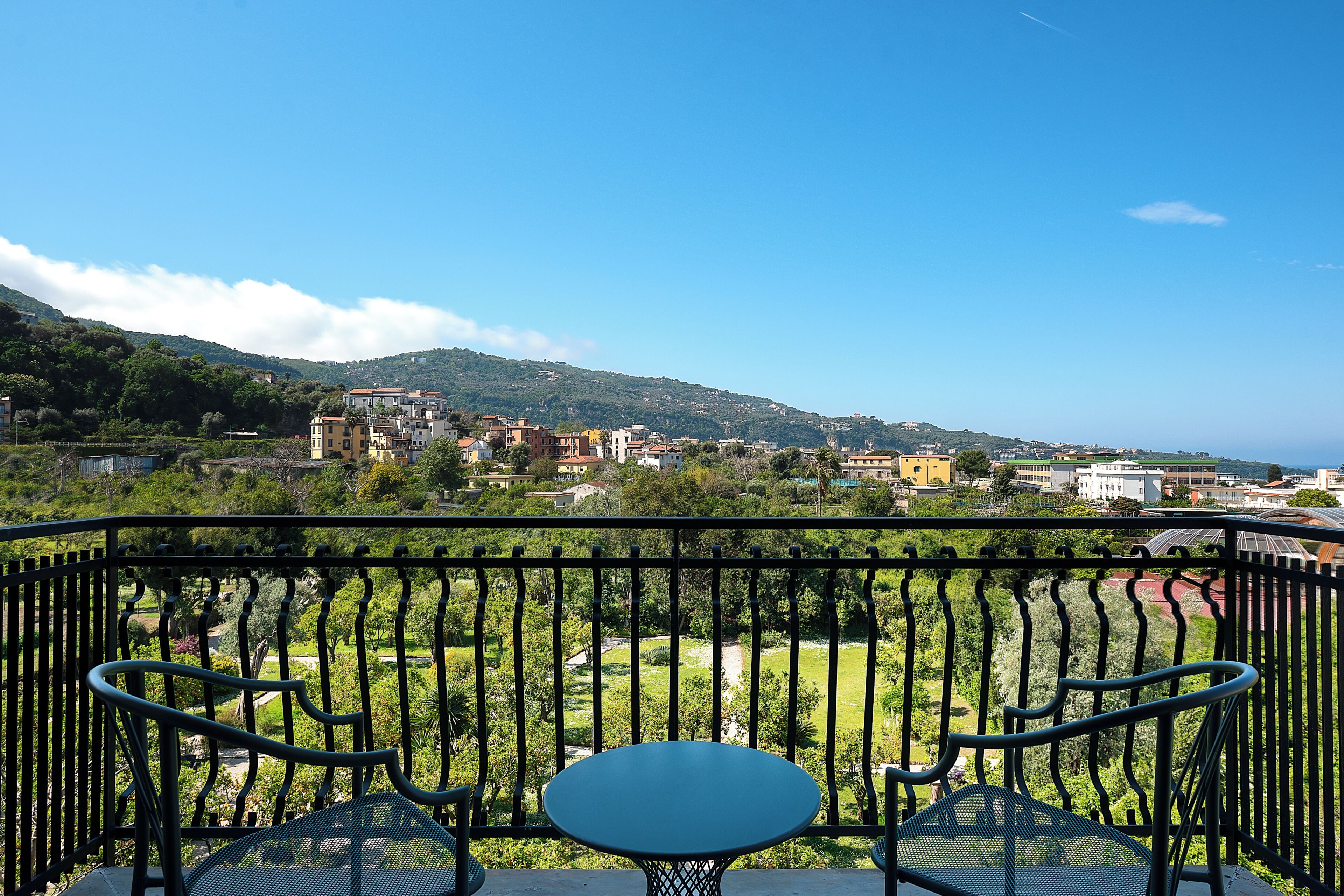 Un balcon avec une table et des chaises, donnant sur un paysage verdoyant et des bâtiments.