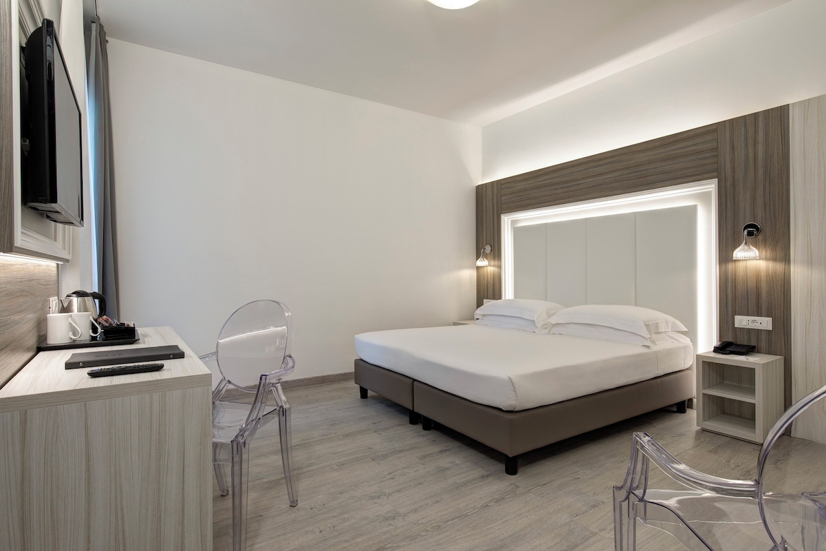 A modern hotel room with a bed, a desk, a chair, and a TV.