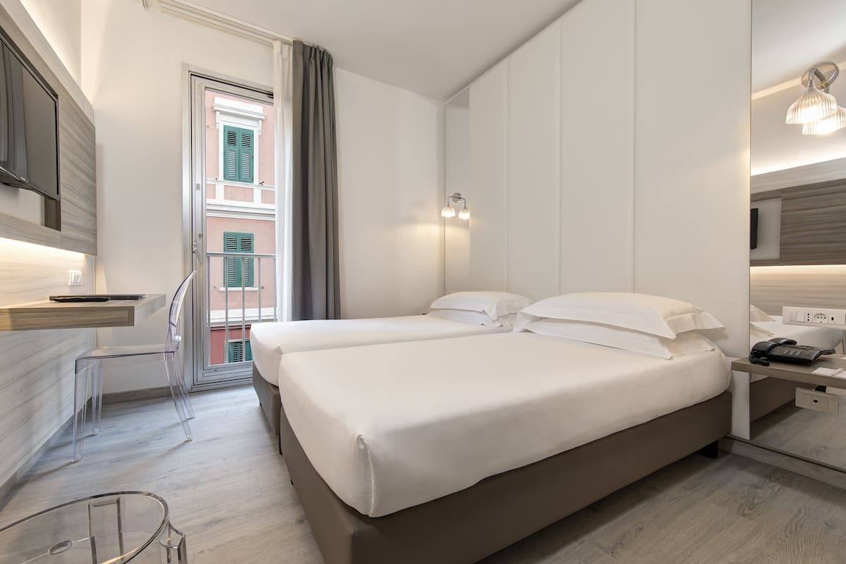 A modern hotel room with two beds, a desk, a chair, and a bathroom.