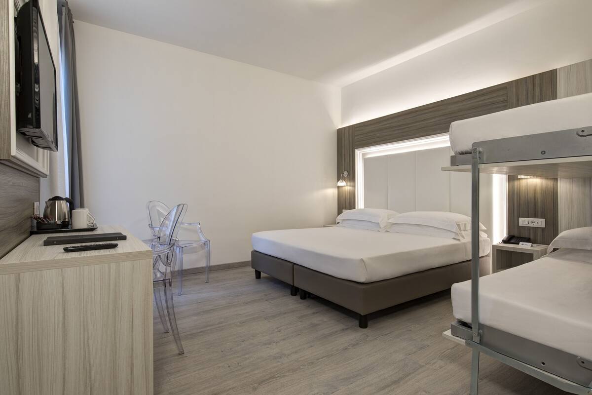 A hotel room with a desk, two beds, a TV, and a mirror.