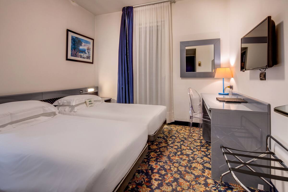 A hotel room with two beds, a desk, a chair, a mirror, and a television.