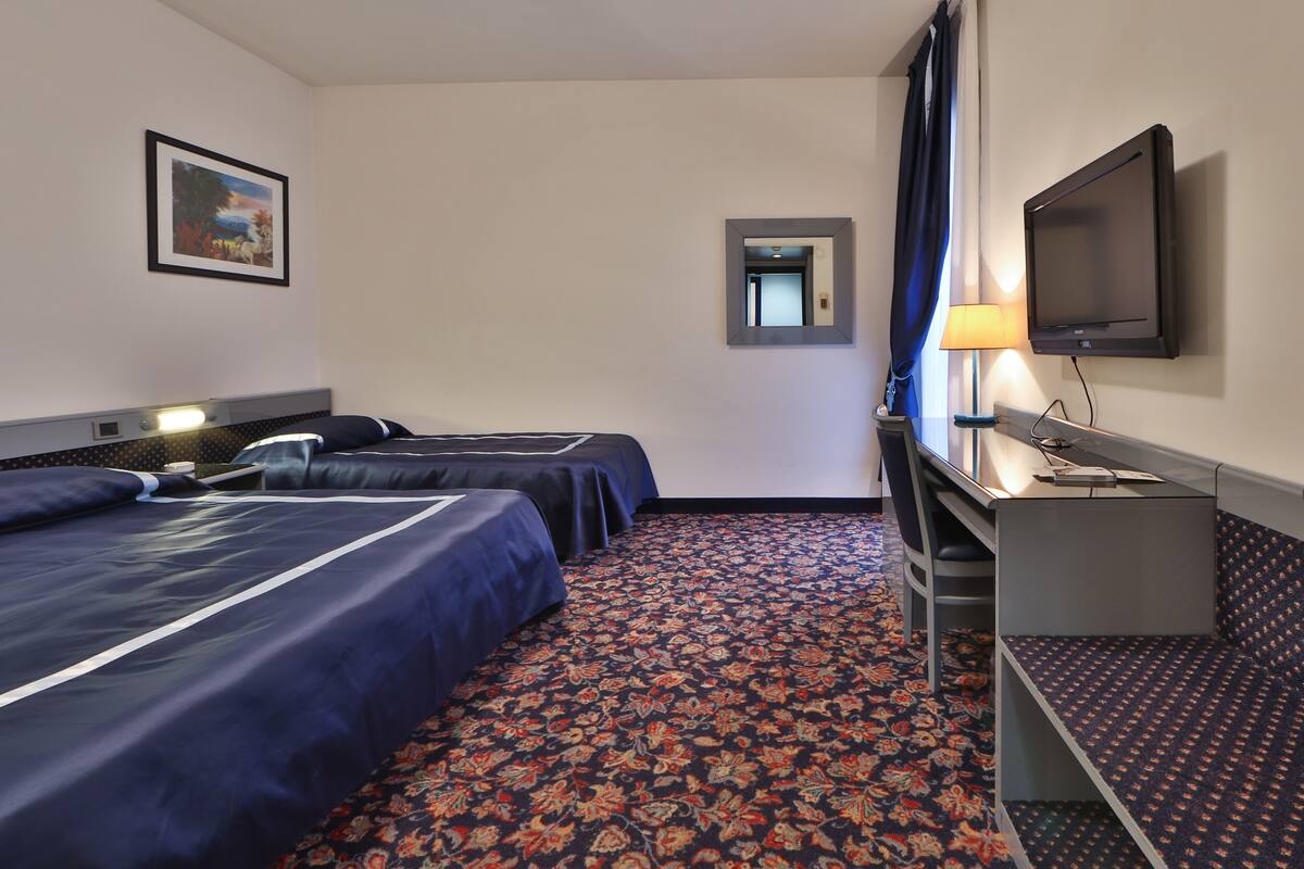A hotel room with two beds, a desk, a TV, and a mirror.